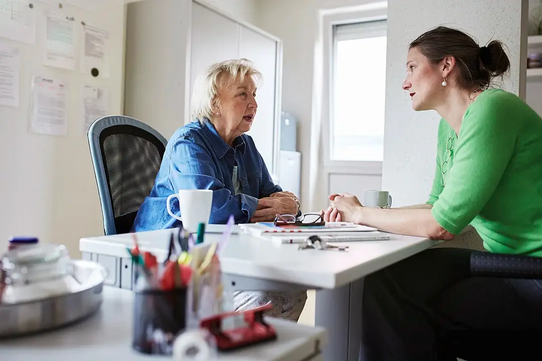 Zwei Frauen sitzen sich an einem Schreibtisch gegenüber und führen ein konzentriertes Gespräch – die Szene steht für Verantwortung, Vertrauen und professionelle Begleitung. Eine Ausbildung oder ein Studium bei der Lebenshilfe Herford bietet nicht nur fachliche Tiefe, sondern auch echte Sinnhaftigkeit im Arbeitsalltag.