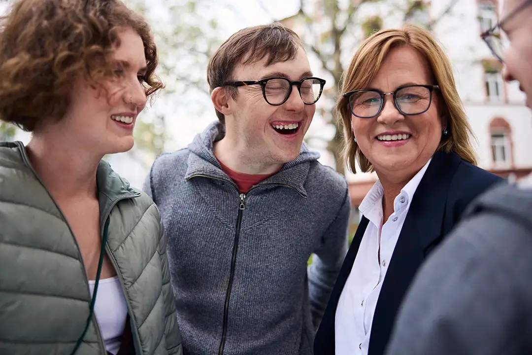 Eine bunt gemischte Gruppe steht draußen zusammen, lacht und blickt sich gegenseitig an – ein Moment voller Offenheit, Nähe und Teamgeist. Wer bei der Lebenshilfe Herford mit einem Direkteinstieg starten möchte, findet hier ein herzliches Umfeld, das Vielfalt lebt.