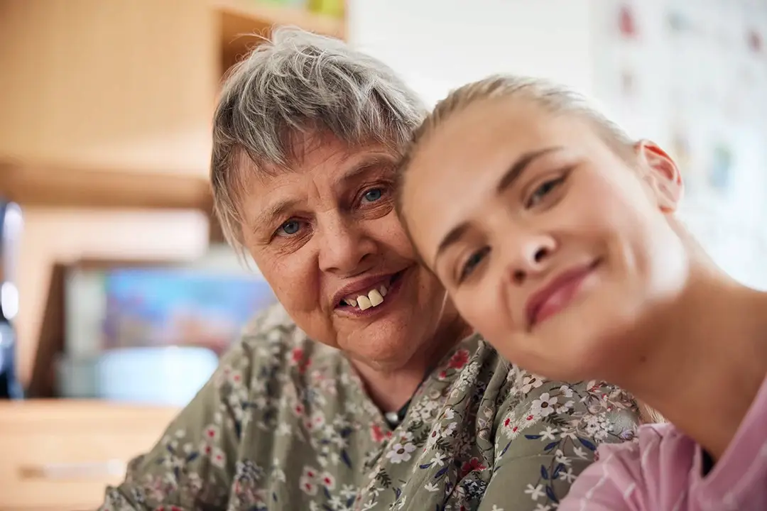 Eine ältere Frau und eine junge Frau lehnen lächelnd die Köpfe aneinander – ein stiller, aber starker Ausdruck von Vertrauen und Menschlichkeit. Wer mit Herz in den Beruf starten möchte, findet beim Direkteinstieg bei der Lebenshilfe Herford echte Nähe und Sinn im Alltag.