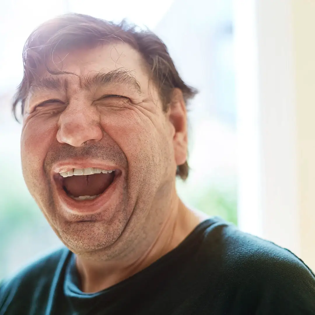 Ein Mann mit Behinderung lacht herzlich in die Kamera – ein Moment voller Lebensfreude und Offenheit, wie sie bei der Lebenshilfe Herford jeden Tag gelebt wird.