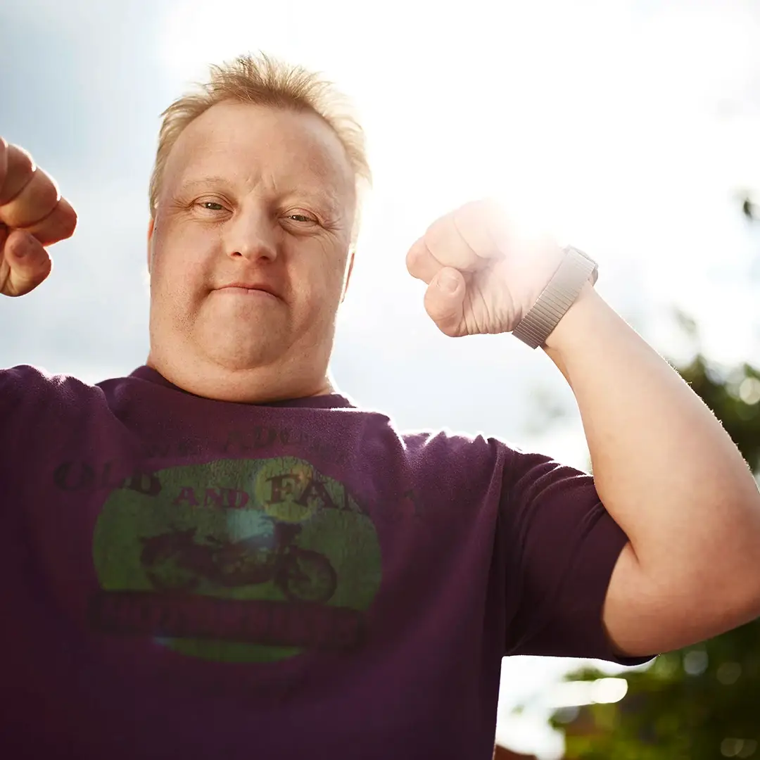 Ein selbstbewusster Mann mit Down-Syndrom zeigt stolz seine Muskeln und blickt direkt in die Kamera – ein ausdrucksstarkes Symbol für Stärke und Selbstbestimmung bei der Lebenshilfe Herford.