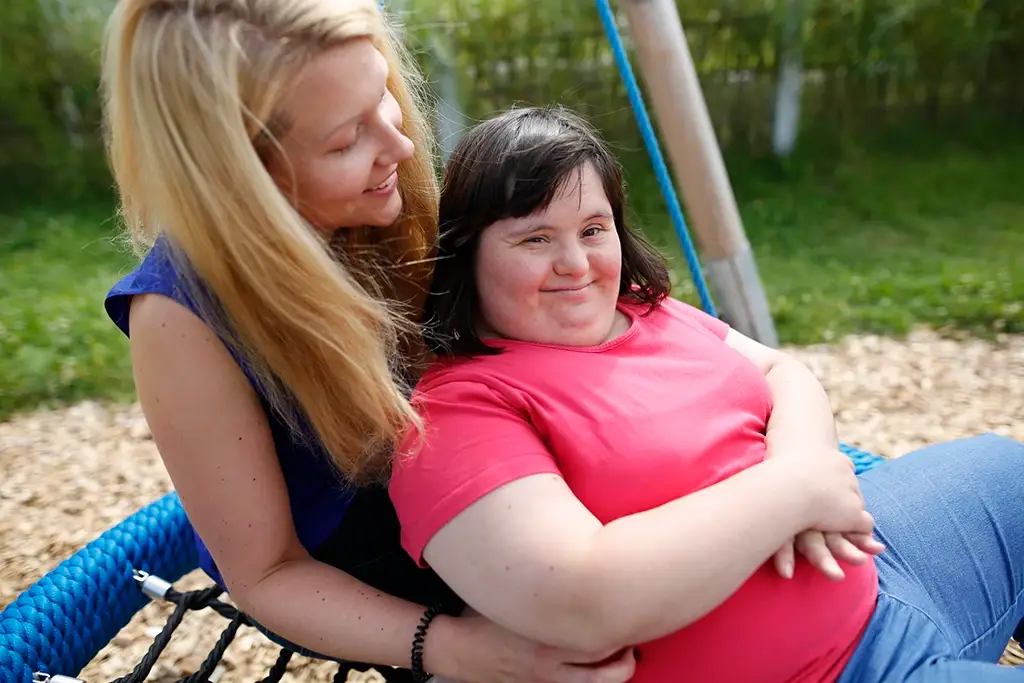 Eine Praktikantin sitzt mit einer jungen Frau mit Behinderung auf einer Schaukel und lacht herzlich mit ihr. Beide wirken entspannt und fröhlich. Das Bild zeigt Nähe, Vertrauen und echte Verbundenheit – Werte, die die Karriere bei der Lebenshilfe Herford auszeichnen.