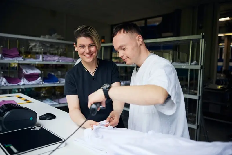 Mitarbeiterin begleitet jungen Mann bei der Arbeit in einer Wäscherei.